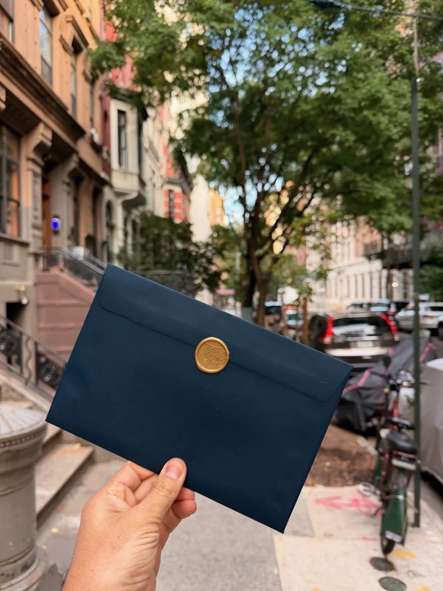 A blue envelope with a gold wax seal on a tree-lined New York street